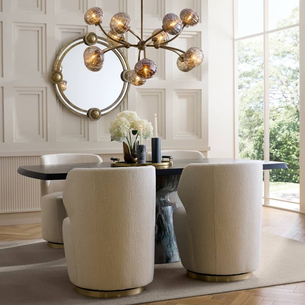 Modern dining room with round mirror, chandelier, and upholstered chairs.