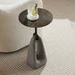 Small round side table with a glass of water on a carpeted floor.