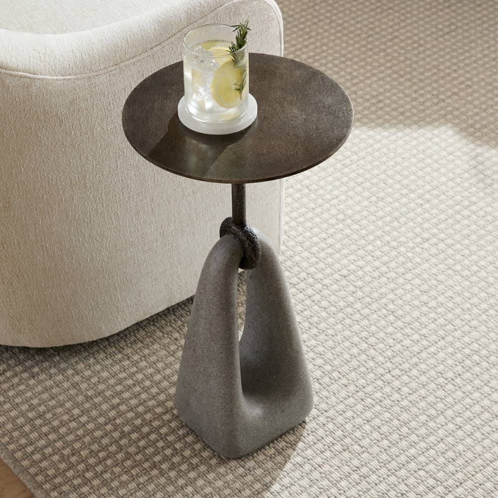 Small round side table with a glass of water on a carpeted floor.