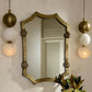 Decorative mirror with gold frame on a wall with pendant lights and plants.