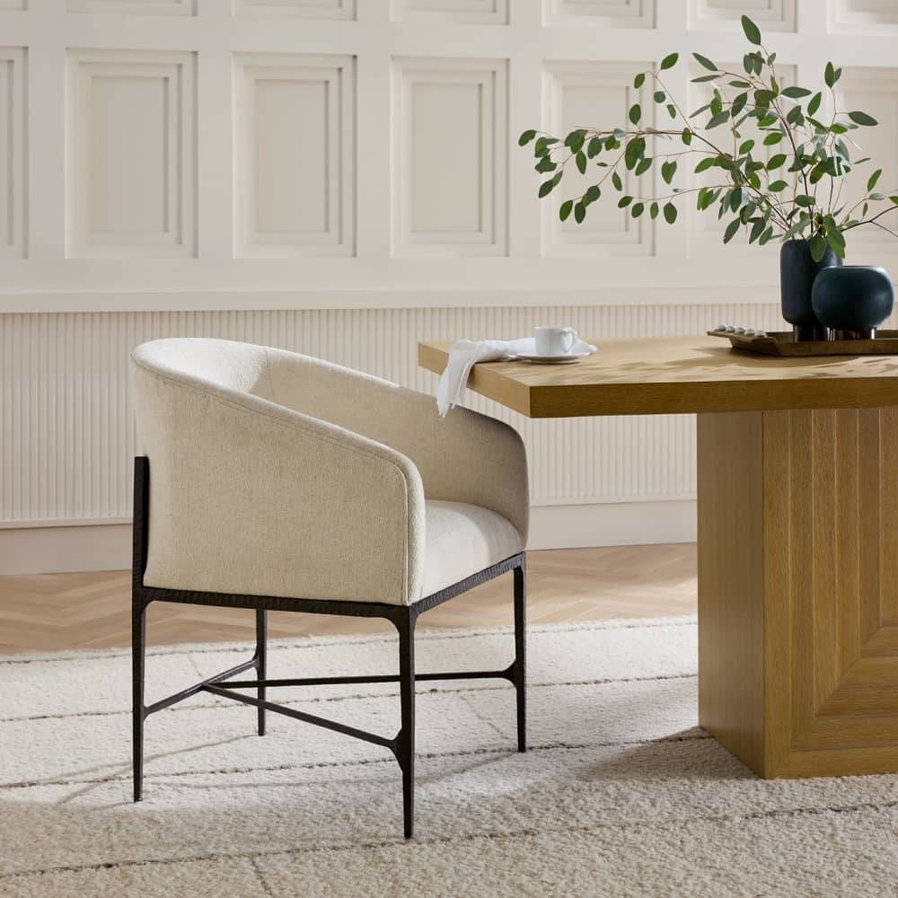 Beige chair in front of a wooden dining table with a plant in the background