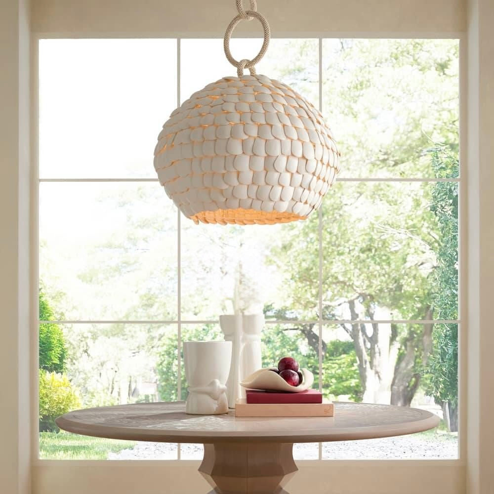 Round dining table with a decorative pendant light in a bright room with large windows.