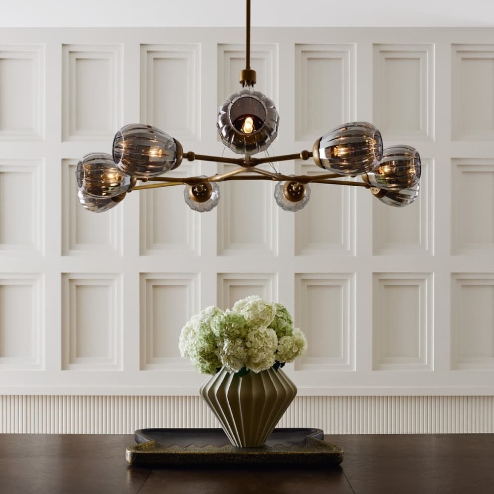 Modern chandelier with smoked glass shades above a vase of flowers on a wooden surface.