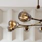 Modern chandelier with glass globe shades and gold branches against a white paneled wall.