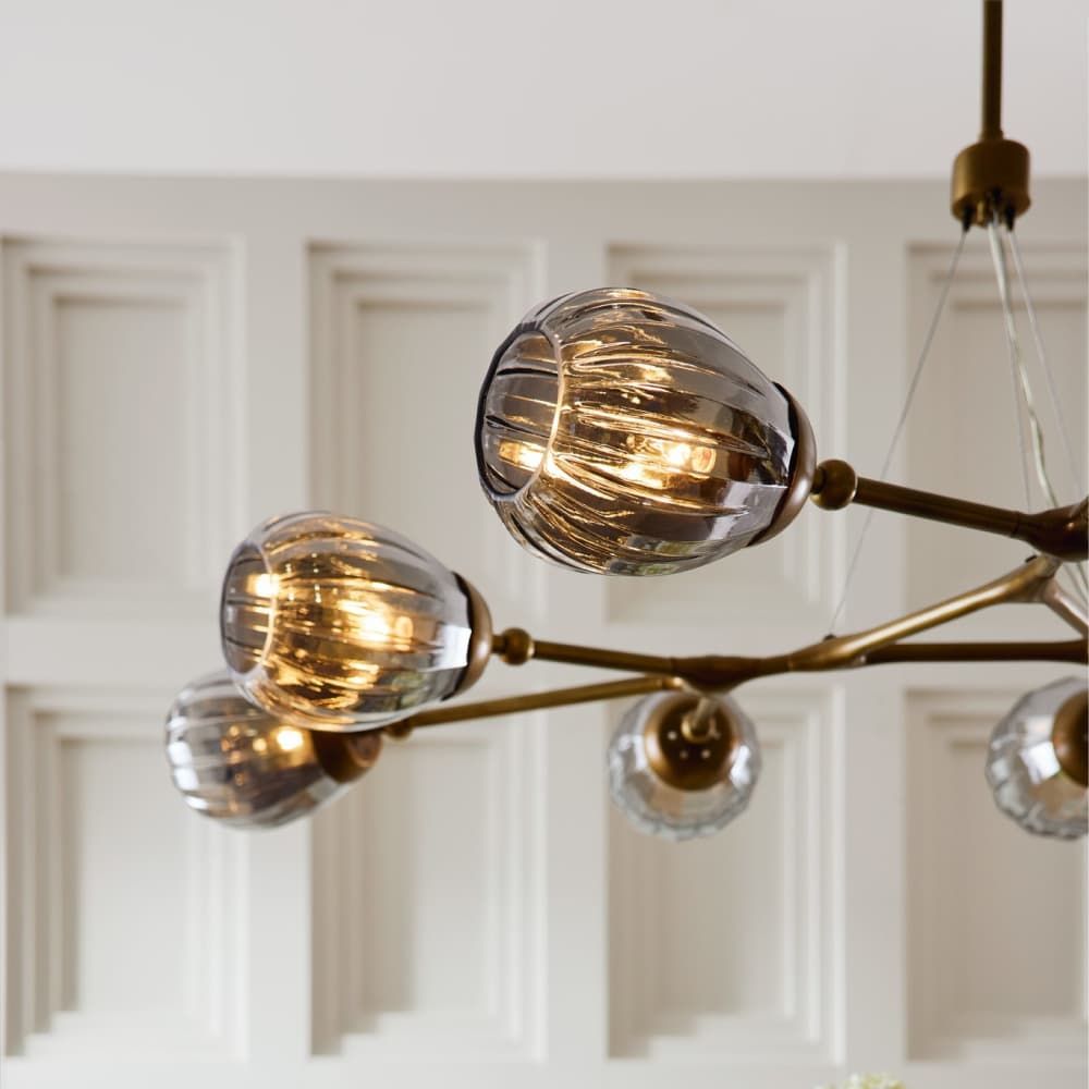 Modern chandelier with glass globe shades and gold branches against a white paneled wall.