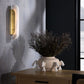 Decorative vase with dried plants on a wooden surface next to a wall sconce.