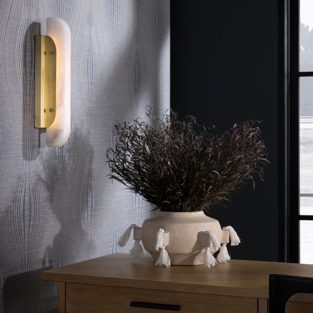 Decorative vase with dried plants on a wooden surface next to a wall sconce.
