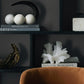 Decorative shelf with books, sculptures, and a chair in a dark room.