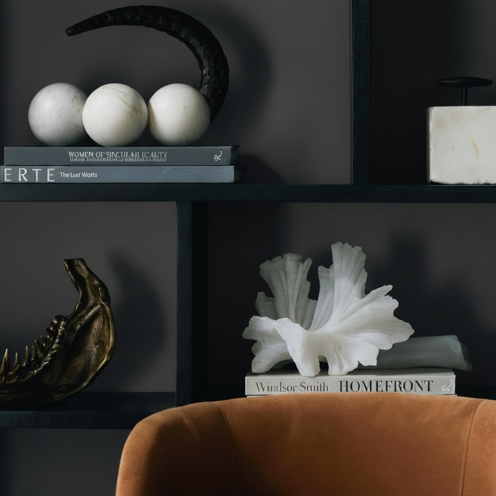 Decorative shelf with books, sculptures, and a chair in a dark room.