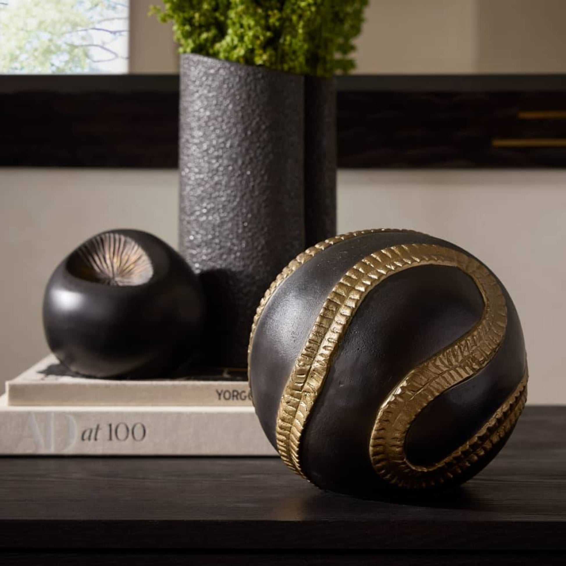 Decorative black and gold sphere on a surface with books and a vase in the background.