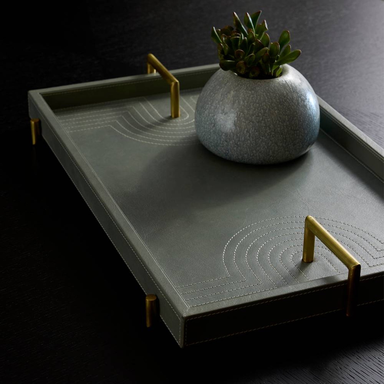 Gray tray with gold handles and a decorative pot on a dark background
