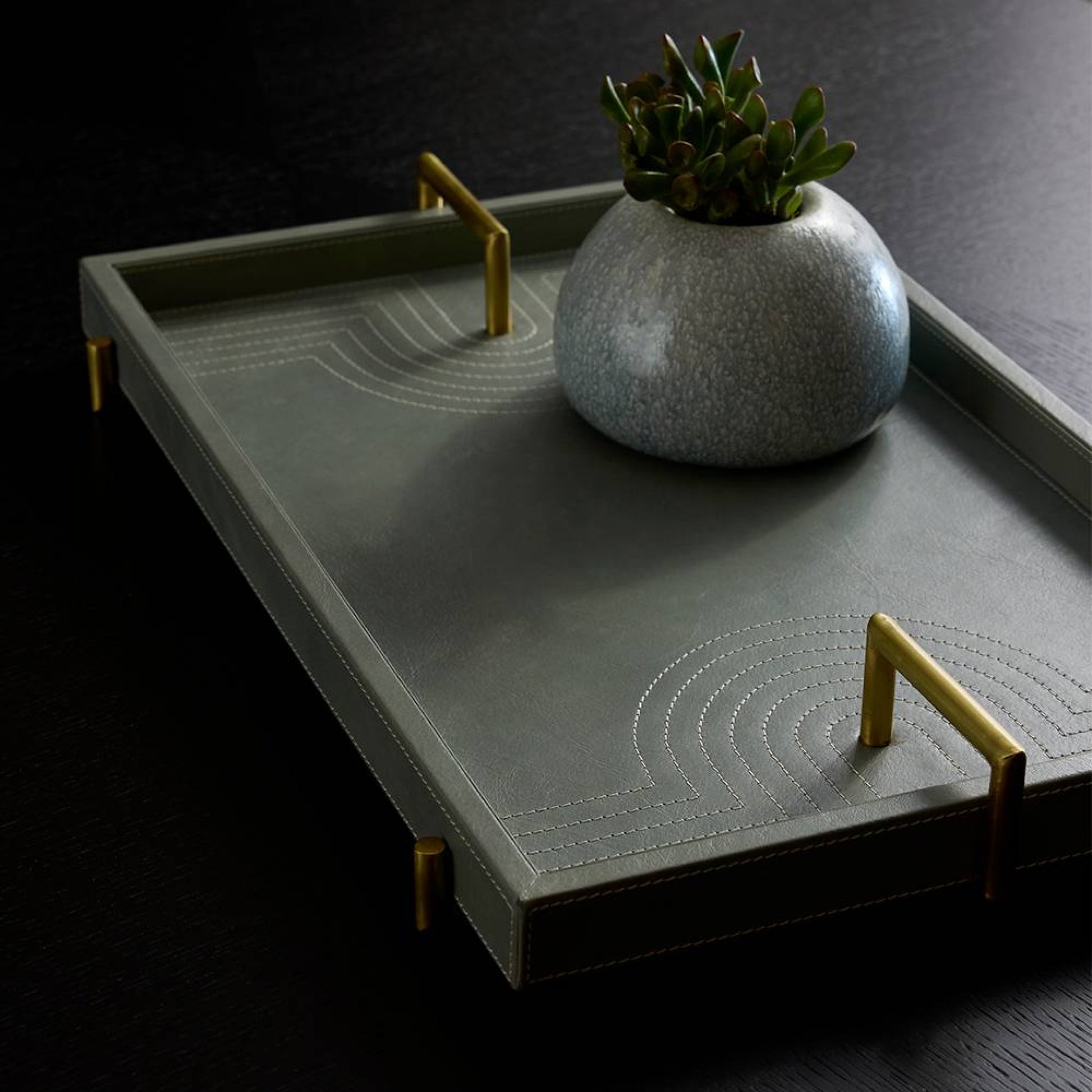 Gray tray with gold handles and a decorative pot on a dark background