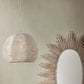 Decorative pendant light and round mirror with wooden frame on a beige wall.