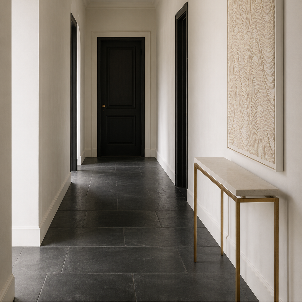 A long hallway with dark charcoal tile flooring, white walls, black doors, a gold chandelier, a large textured beige wall art piece, and a console table with a white top and gold frame.