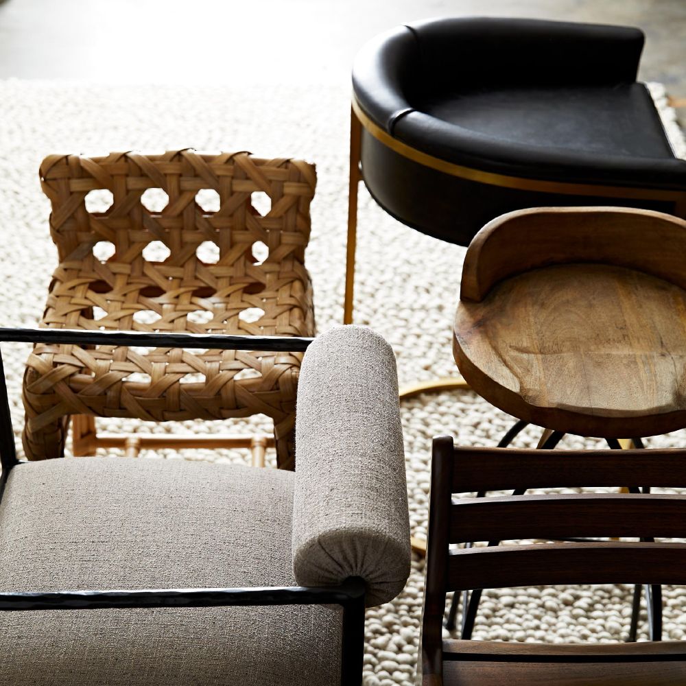 Collection of chairs including a woven chair, gray upholstered chair, and wooden chair with a black cushion.