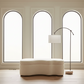 Modern interior with a white ottoman and floor lamp against a wall with arched windows.