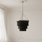 Black chandelier hanging in a room with white walls and curtains.