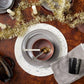 Dining table setting with gray plates, pink bowl, gold fork, and silver spoon on a wooden surface with tinsel.