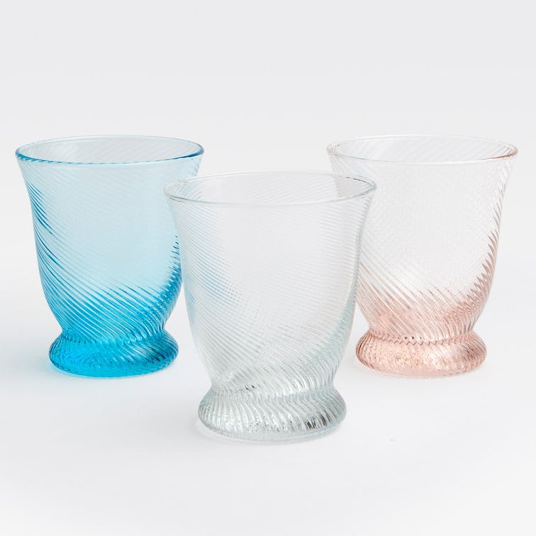 Three textured glass tumblers with spiral ridges, shown in blue, clear, and pale pink on a white background.