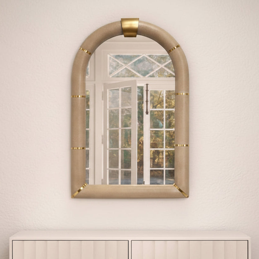 Beige dresser with gold accents and an arched mirror above it against a white paneled wall.