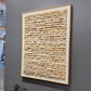 Framed textured artwork on a gray wall with sculptures below.