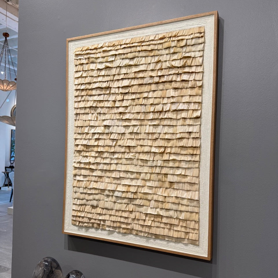 Framed textured artwork on a gray wall with sculptures below.