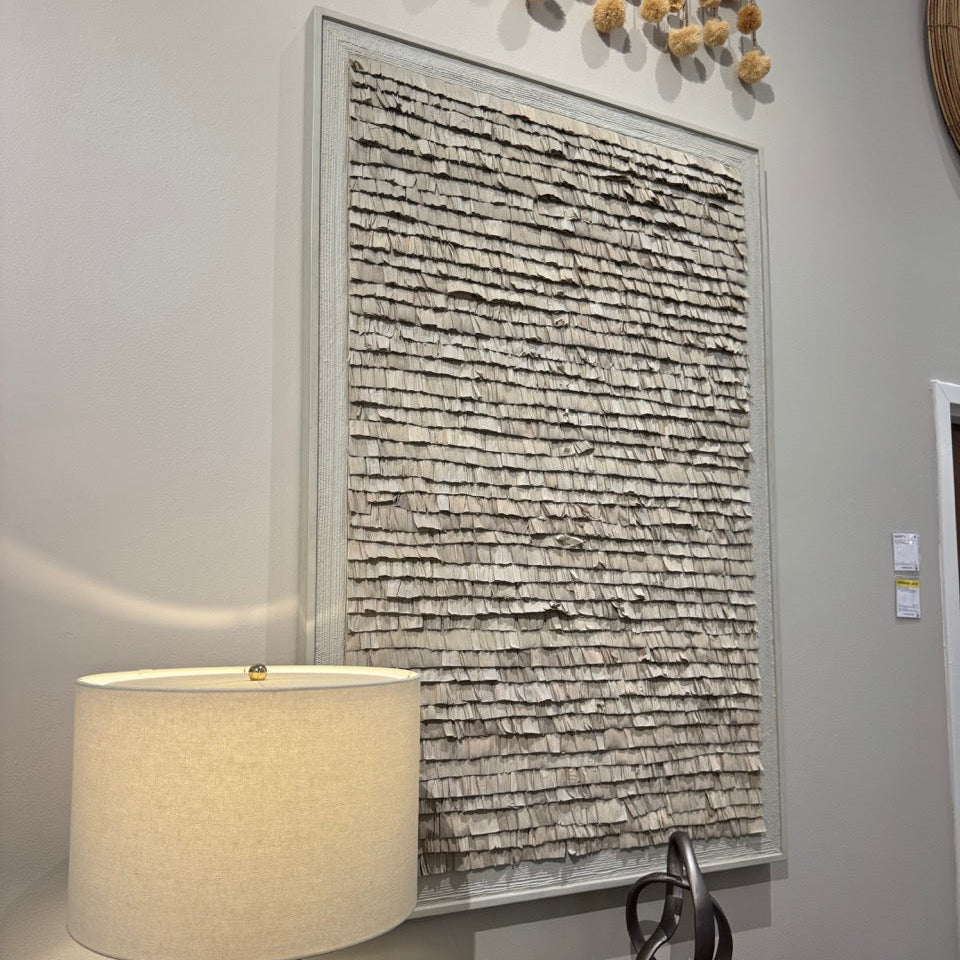 Decorative wall art with a textured pattern on a gray wall, accompanied by a lamp and small sculptures.