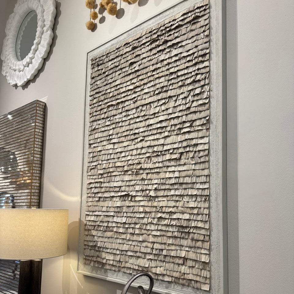 Decorative wall art with a textured design on a gray wall, next to a lamp and small sculpture.