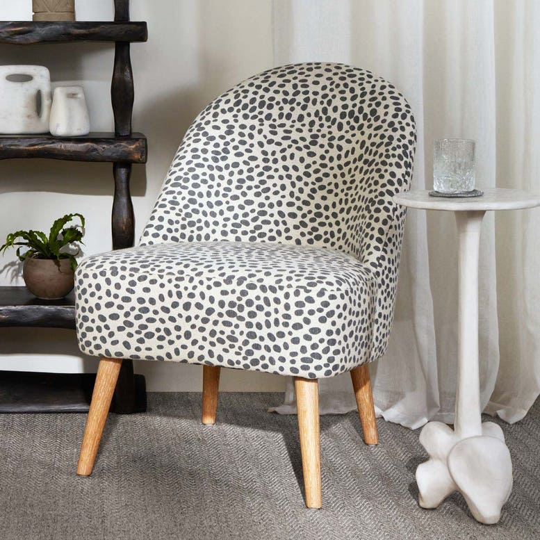 Chair with a patterned cover in a room setting with a shelf and small table.