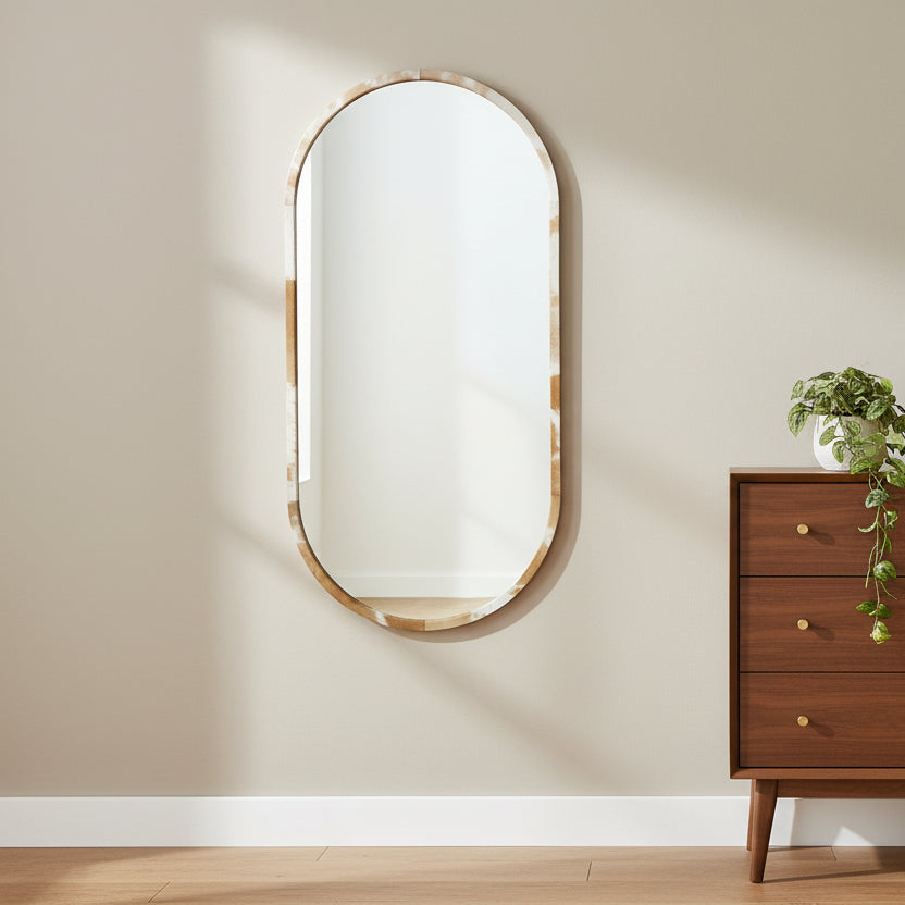 Wooden dresser with a plant and decorative item next to an oval mirror on a beige wall.