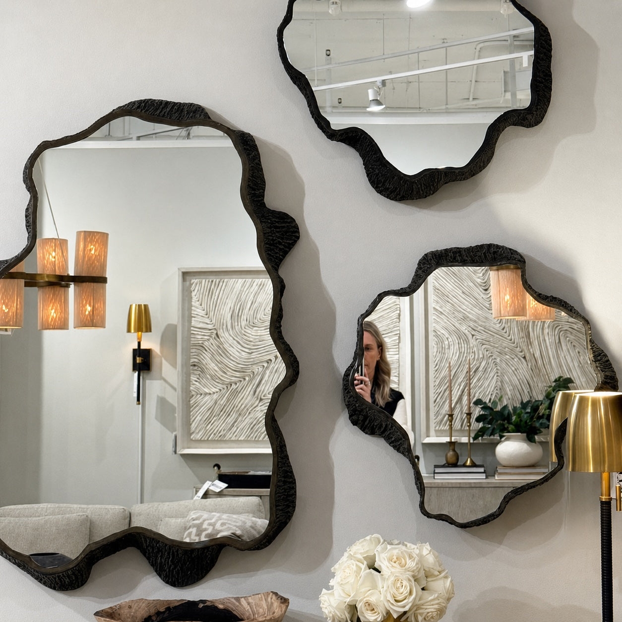 Three organic-shaped black textured mirrors with irregular scalloped edges, displayed on a white wall in a modern room setting.