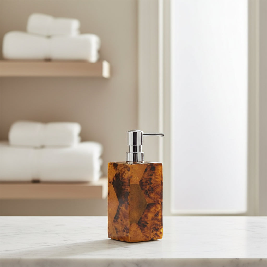 A rectangular soap dispenser bottle made of faceted amber-brown stone with a polished silver pump dispenser, shown on a light gray background.
