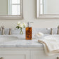 A rectangular resin soap dispenser with a polished silver pump, featuring a marbled amber and brown pattern on a light gray background.