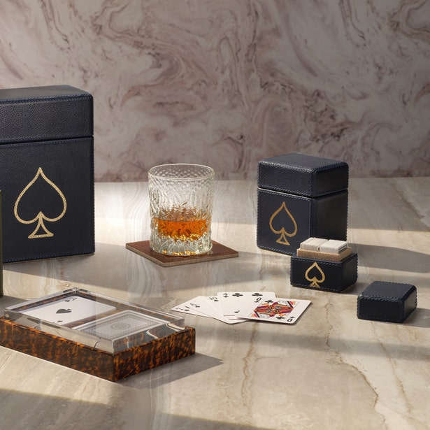 Card game set with playing cards, card holder, and glass of whiskey on a marble surface.