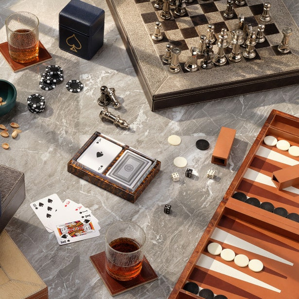 Tabletop games including chess, backgammon, and cards with drinks on a marble surface.