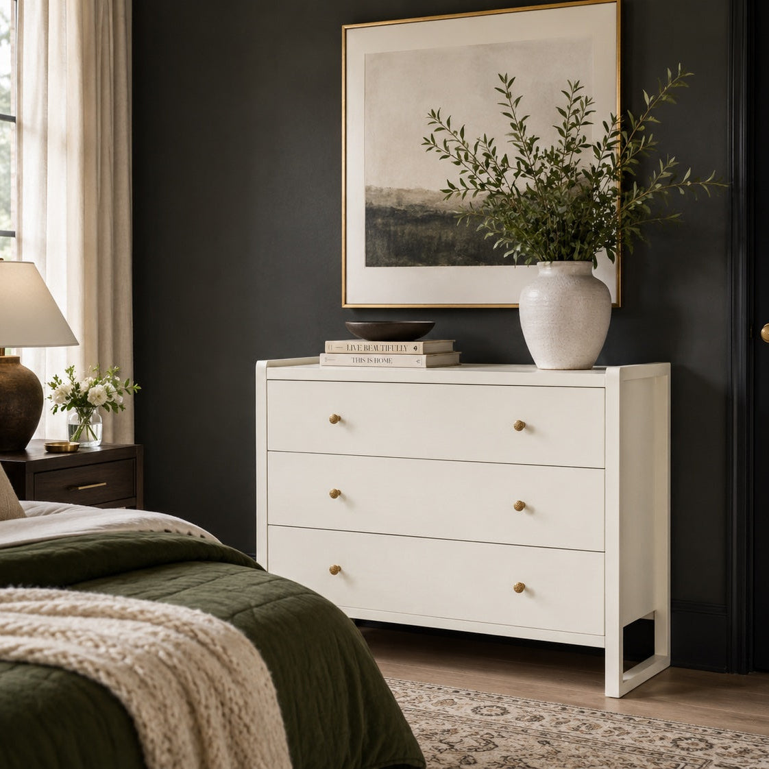 white dresser in a bedroom against a dark green wall with a vase and books on top of it