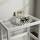 White side table with a black and white striped tray holding decorative items against a plain wall.