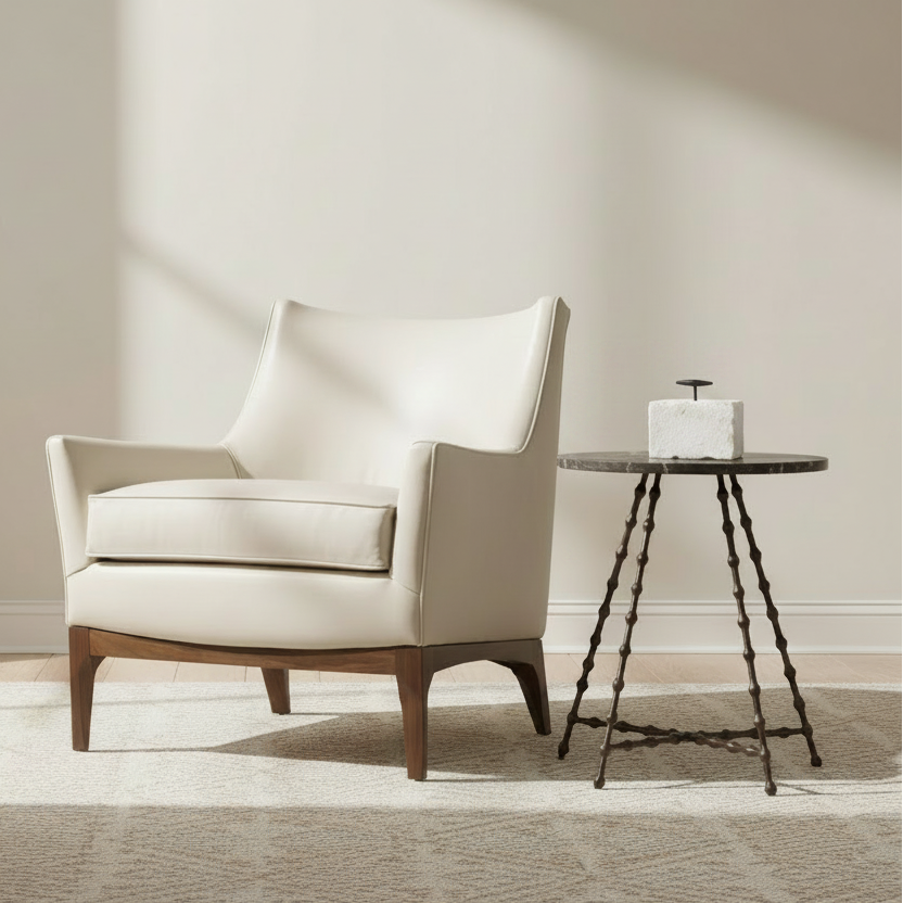 A cream-colored leather armchair with a wooden base sits on a light rug next to a small round side table in a bright, modern room with natural sunlight.