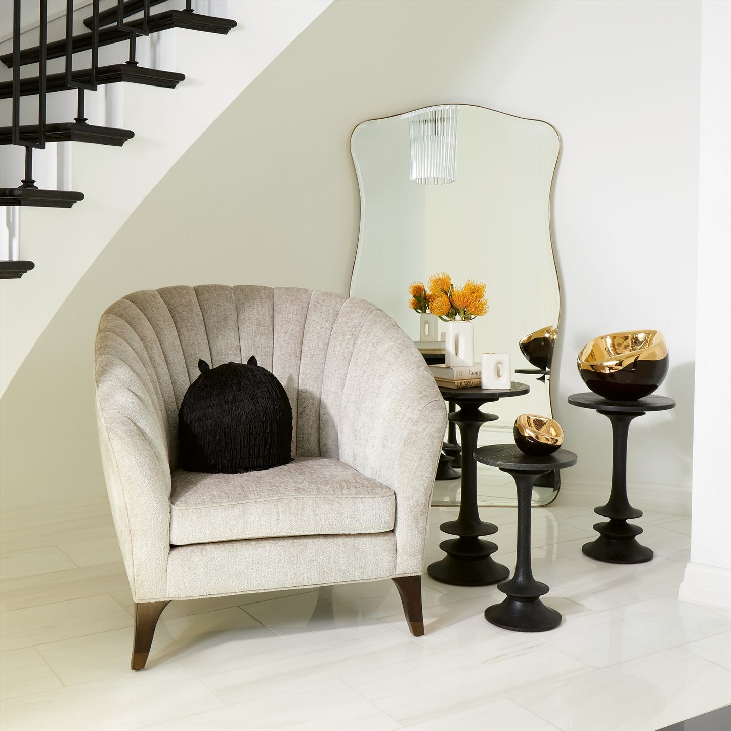 Decorative room with a beige armchair, black side tables, and a large mirror.