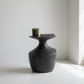 Dark gray ceramic vase with a candle and book on a white surface