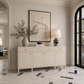 A cream-colored wooden console cabinet with gold knobs, styled in a bright, elegant entryway with a vase, books, a lamp, and a large framed abstract print on a tiled floor.