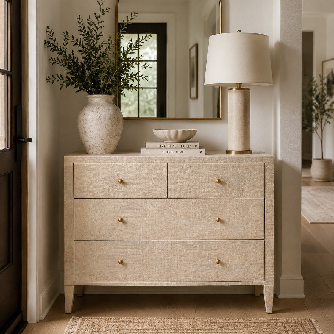 dresser gold in an entryway with a mirror above it and a lamp, vase and books on top