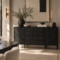 A black wood sideboard or credenza with brass drawer knobs, styled in a modern dining room setting with a vase of greenery, candles, and wall sconces.