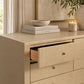 A gold/beige textured dresser with an open drawer, styled with books, a bowl, a candle, and a vase in a warm, elegant room setting.