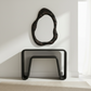 Modern black console table with unique mirror above it against a white wall.