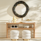Decorative console table with round mirror and white stools in a room setting