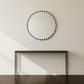 Round mirror with decorative border on a white wall above a dark wooden console table.