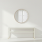 Round mirror with wooden frame on a white wall above a white shelf.