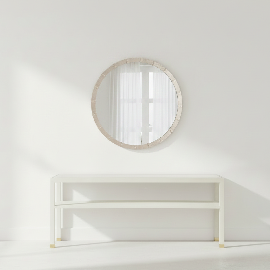 Round mirror with wooden frame on a white wall above a white shelf.