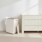 White laundry basket with a white towel inside next to a white dresser.